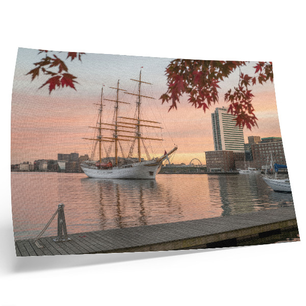 Poster Um veleiro ao pôr do sol, um panorama tranquilo da cidade.