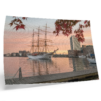 Poster Um veleiro ao pôr do sol, um panorama tranquilo da cidade.