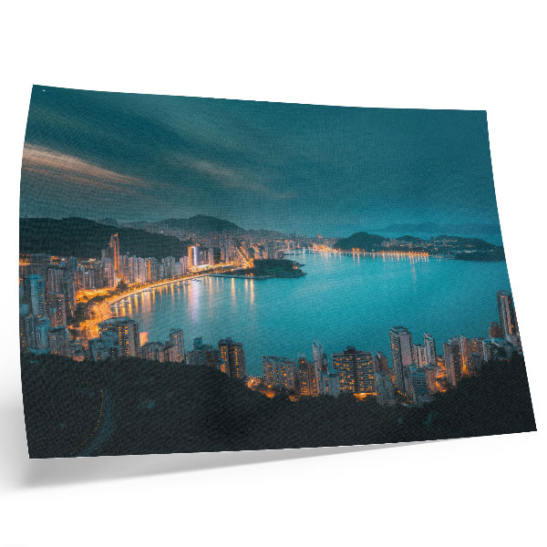 Poster em tela Vista noturna da cidade sobre a água, com arranha-céus luminosos.